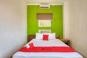 a bedroom with a green wall and a bed with red pillows at RedDoorz near Bali Zoo Ubud in Sukawati