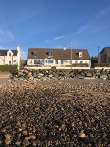 a pile of rocks on a beach with a house in the background at Old Police House in Aultbea