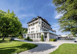 un grand bâtiment blanc dans un parc arboré dans l'établissement Grand Hôtel des Rasses & Wellness, à Les Rasses