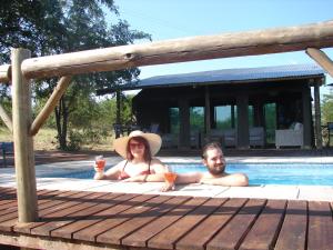 un hombre y una mujer sentados en una piscina con copas de vino en Camp Bethel, en Hoedspruit