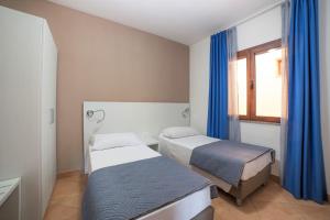 a bedroom with two beds and a window with blue curtains at Babai Village Resort in Tertenìa