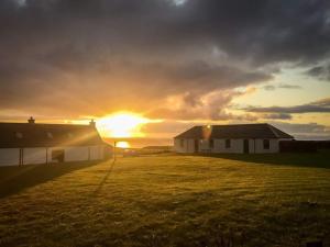 a sunset over two houses in a field with the sun setting at Monkstadt No 6 -Jessie's Hideaway in Portree