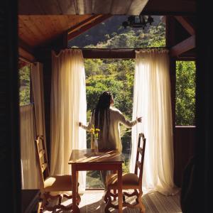 a woman standing at a table looking out of a window at Reserva Três Picos Chalés in Nova Friburgo