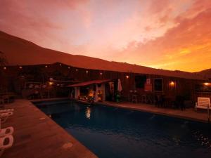 a swimming pool in front of a building with a sunset at Ecocamp Huacachina in Ica