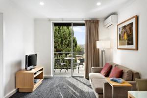 a living room with a couch and a tv and a balcony at Quest St Kilda Bayside in Melbourne
