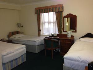a hotel room with two beds and a desk and a mirror at Abbey Lodge Hotel in High Wycombe