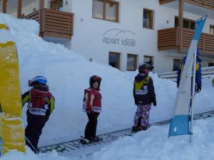 three children standing in the snow in front of a snow ramp at Apart Ideal in Lermoos