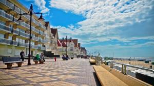 people sitting on benches on a sidewalk near the beach at Strandvakantieappartement Zilverstrand - met binnenzwembad! in De Haan