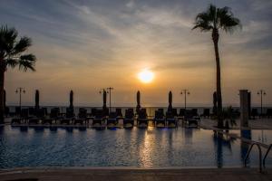 een zwembad met stoelen en palmbomen bij zonsondergang bij Neopol Hotel in Kuşadası