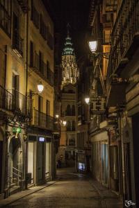 eine leere Straße in der Nacht mit einem Uhrturm im Hintergrund in der Unterkunft Hostal la posada de Zocodover in Toledo