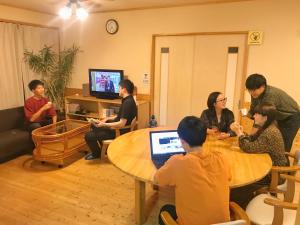 um grupo de pessoas sentadas em torno de uma mesa com um laptop em HIBARI GUESTHOUSE em Sendai