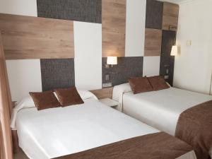 two beds in a hotel room with white sheets and brown pillows at Cesar Augustus in Cambrils