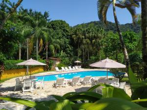 a resort pool with chairs and umbrellas and palm trees at Chalé Pousada da Aldeia in Boicucanga
