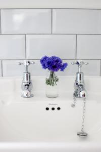 - un lavabo blanc dans la salle de bains avec un vase de fleurs violettes dans l'établissement Cromhall Farm, à Chippenham