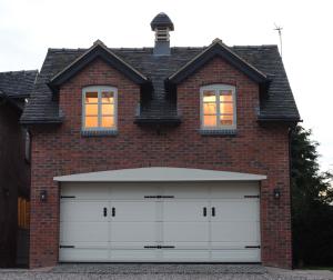 uma casa de tijolos com duas portas de garagem brancas em Woodleighton Cottages em Uttoxeter