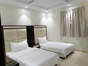 two beds in a room with white walls and a window at Fakhamat Al Orjoana & Suites in Sakakah