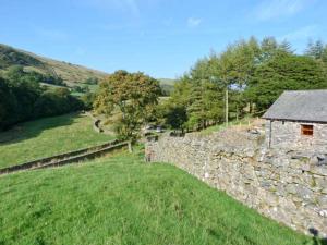 eine Steinmauer und ein Gebäude auf einem Feld in der Unterkunft Copper Beech Cottage in Coniston