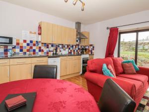 ein Wohnzimmer mit einem roten Sofa und einer Küche in der Unterkunft Stables Cottage in Llanrwst