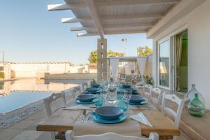 een houten tafel met witte stoelen en een tafel met glazen bij Villa Niraclò by Raro Villas in Carovigno