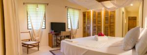 a bedroom with a white bed with a chair and a television at Palm Garden Boutique Hotel in Watamu