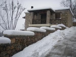 a house covered in snow with a stone wall at AELIA HOME in Synikia Mesi Trikalon
