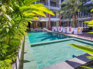 a swimming pool at a hotel with white chairs and trees at Grand Mirah Boutique Hotel in Denpasar