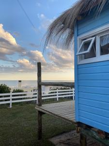 a blue shack sitting on a wooden boardwalk next to the ocean at Cabañas Punta Papaya in Punta Del Diablo