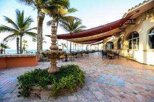 un patio con mesas, sillas y palmeras en Buena Vista Oceanfront & Hot Springs Resort en Buenavista