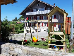 a play house with a swing in front of a house at Gästehaus Gitti Dorner in Hittisau