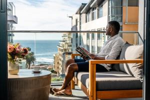 a man sitting on a chair reading a book on a balcony at Latitude Aparthotel by Totalstay in Cape Town
