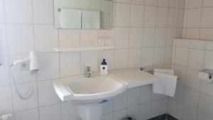 Baño blanco con lavabo y espejo en Pension Villaggio, en Mertesheim