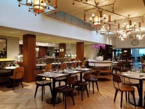 uma sala de jantar com mesas, cadeiras e lustres em The Athenaeum Hotel & Residences em Londres