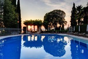 a swimming pool with blue water and trees at Villa Cortine Palace Hotel in Sirmione