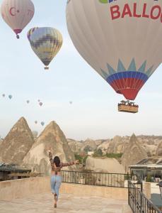 a woman is running in front of hot air balloons at Kismet Cave Mansion in Göreme