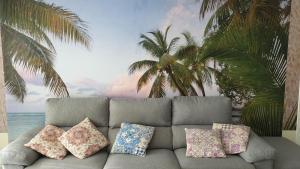 un sofá con almohadas frente a un mural de palmeras en CanariasBrisaMar - Apartamento, en Arinaga