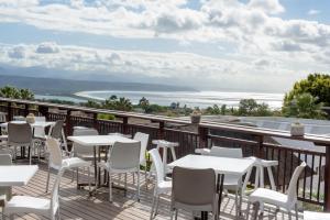 un patio con mesas blancas y sillas en el balcón en Whalesong Hotel & Spa, en Plettenberg Bay