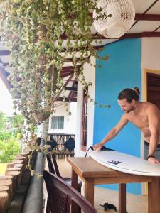 un hombre parado en una mesa con una tabla de surf en HappyShack Hostel, en Mirissa
