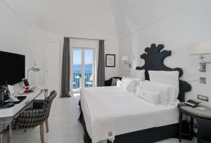a white bedroom with a bed and a desk with a computer at Hotel Villa Franca in Positano