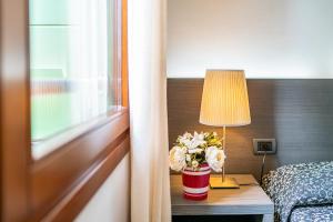 a hotel room with a bed and a table with a lamp and flowers at Hotel La Pergola in Lignano Sabbiadoro