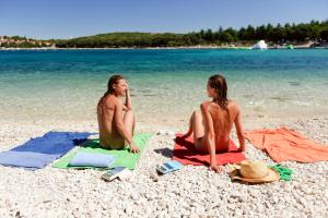 two people sitting on a beach near the water at Maistra Camping Koversada Naturist Mobile homes in Vrsar