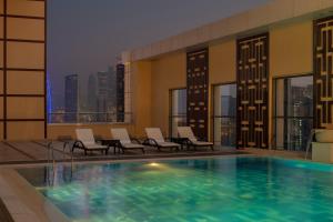 uma piscina do hotel com cadeiras e vista para a cidade em Dusit Doha Hotel em Doha