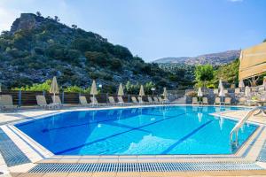 a swimming pool with chairs and a mountain in the background at Villa Mare Monte ApartHotel in Malia