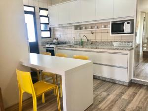 cocina con encimera blanca y sillas amarillas en Apartamento Condominio Maria Isabel, en Florianópolis