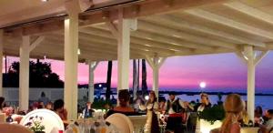 a group of people sitting under a pavilion with a sunset at Hotel Coral Beach in Roda