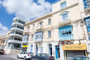 un edificio con ventanas azules y coches aparcados en una calle en Seafront apartment between Valletta and Sliema, en Msida