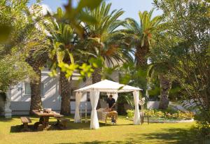 a man sitting under a white tent in a yard with palm trees at Mandraki Village Boutique Hotel in Koukounaries