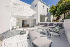 a patio with white furniture and an umbrella at The Little Palm in Bloubergstrand