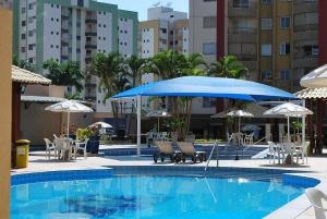 una piscina con sombrilla azul, sillas y sombrillas en Prive das Thermas I - Achei Ferias, en Caldas Novas