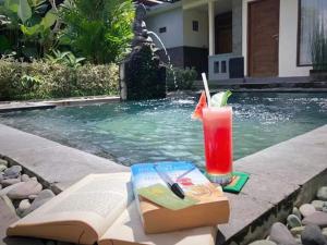 a book and a drink sitting next to a swimming pool at Villa JJ and Spa Ubud in Ubud