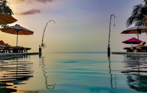 a swimming pool with umbrellas and the ocean at Puri Mas Boutique Resort & Spa in Senggigi